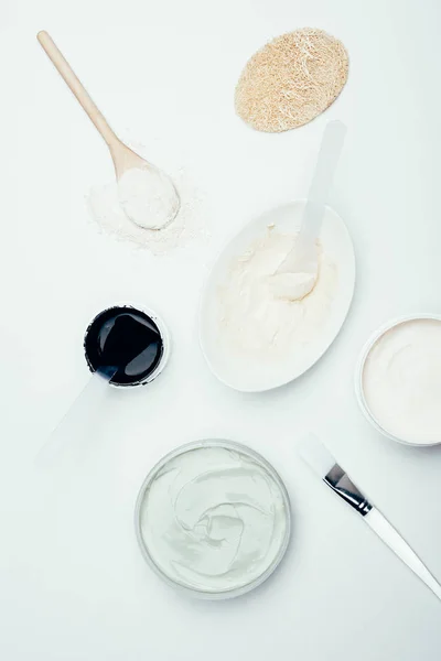 Flat lay with sponge, various clay masks in containers, clay powder, spoons, plate and brush isolated on white surface — Stock Photo