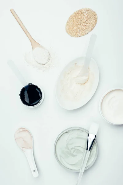 Flat lay with sponge, various clay masks in containers, plate, clay powder, spoons and brush isolated on white surface — Stock Photo