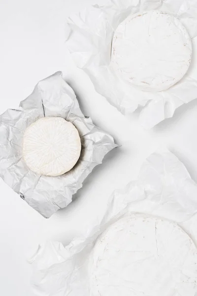 Vista superior de cabeças de queijo brie orgânico em papel amassado e na superfície branca — Fotografia de Stock