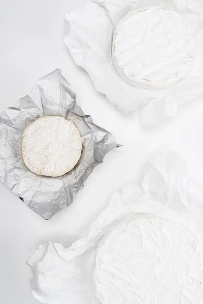 Top view of brie cheese heads on crumpled paper and on white tabletop — Stock Photo