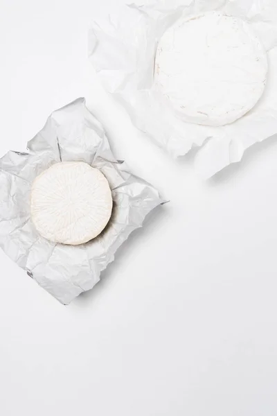 Vue de dessus des têtes de fromage brie sur papier froissé et sur surface blanche — Photo de stock