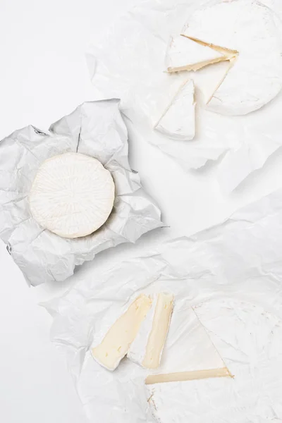 Vista superior de varias cabezas de queso brie sobre papel arrugado y sobre superficie blanca - foto de stock