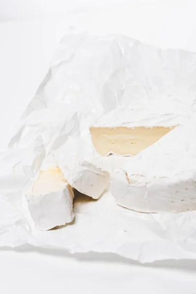 Gros plan du fromage brie tranché sur papier froissé et sur surface blanche — Photo de stock