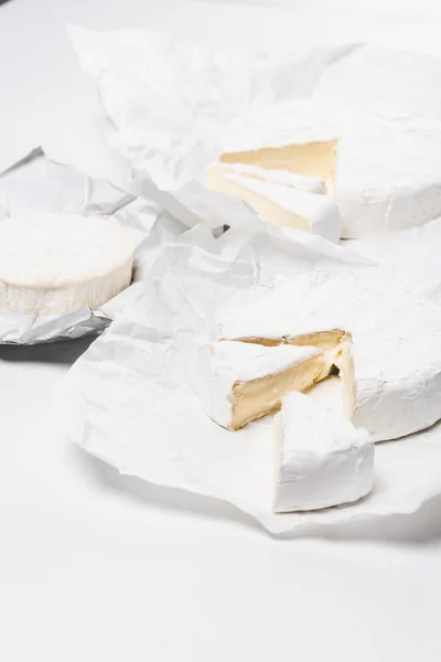 Cabeças de queijo brie fatiadas em papel amassado e na superfície branca — Fotografia de Stock