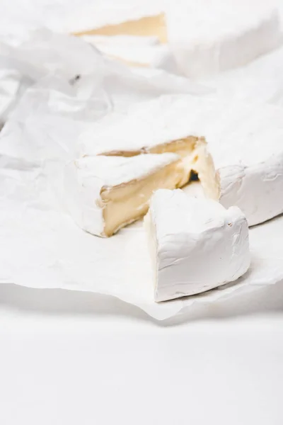 Queso brie en rodajas sobre papel arrugado y sobre superficie blanca - foto de stock