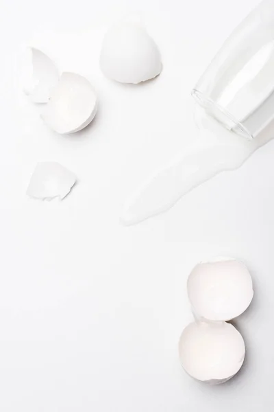 Top view of broken chicken egg shells with spilled milk on white surface — Stock Photo