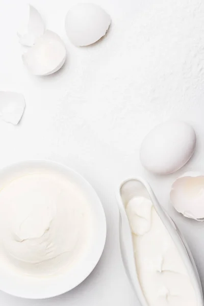 Draufsicht auf saure Sahne und rissige Eierschalen auf weißer Oberfläche mit Mehl verschüttet — Stockfoto