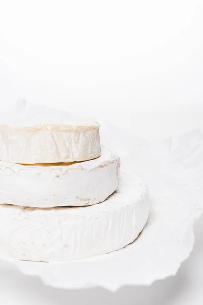 Gros plan de la pile de têtes de fromage brie sur du papier froissé et sur une surface blanche — Photo de stock
