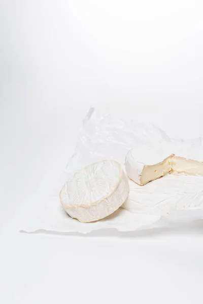 Tiro de close-up de queijo brie em papel amassado e na superfície branca — Fotografia de Stock