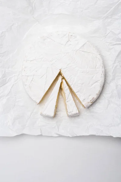 Vista superior de queijo brie fatiado em papel amassado e na superfície branca — Fotografia de Stock