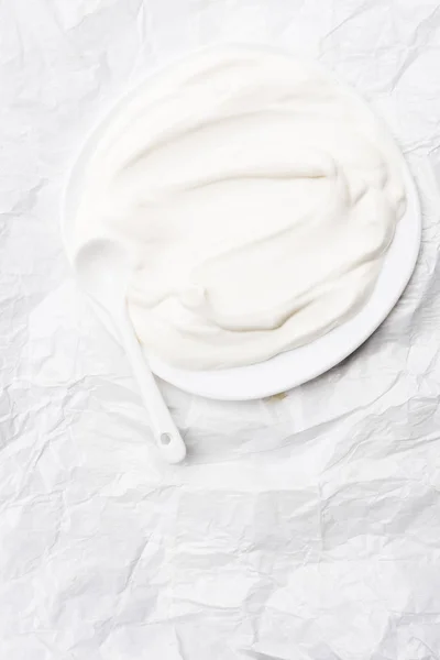 Top view of sour cream on plate with spoon on white crumpled paper — Stock Photo