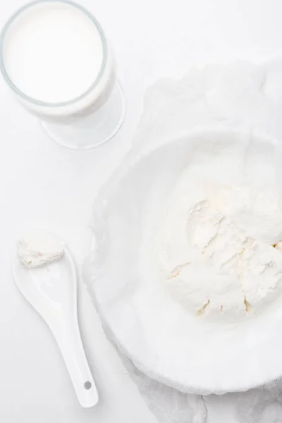 Top view of cottage cheese on cheesecloth glass of milk with spoon on white surface — Stock Photo