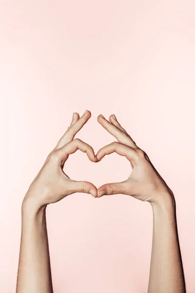 Vista parcial de la mujer haciendo símbolo del corazón por los dedos aislados sobre fondo rosa - foto de stock