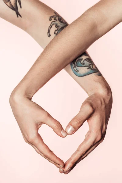 Vista parcial de la mujer y el hombre tatuado haciendo símbolo del corazón por las manos aisladas sobre fondo rosa - foto de stock