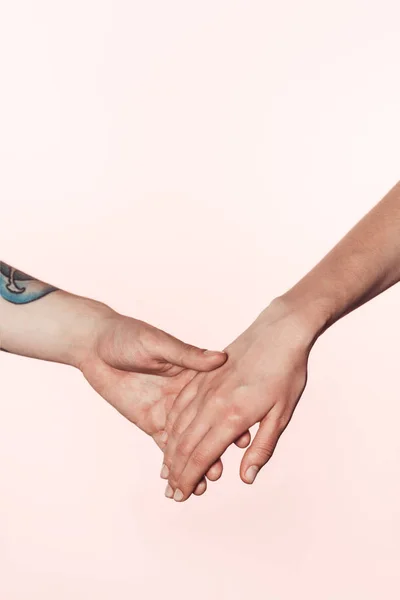 Vue partielle de l'homme et de la femme tatoués tenant les mains isolées sur fond rose — Photo de stock