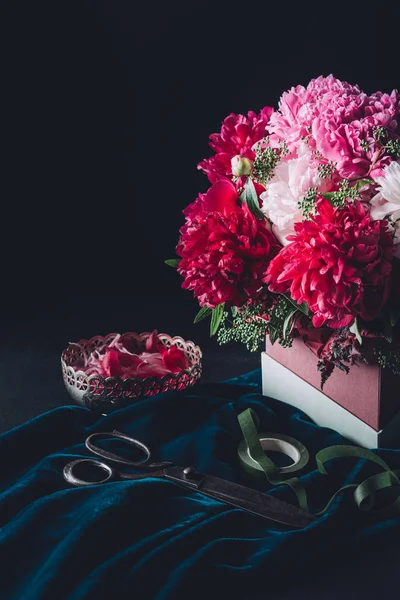 Bouquet of pink peonies with scissors, ribbon and vintage bowl with petals on dark — Stock Photo