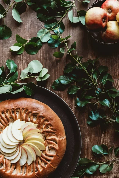 Top view of homemade apple pie and fresh apples with green leaves on wooden tabletop — Stock Photo