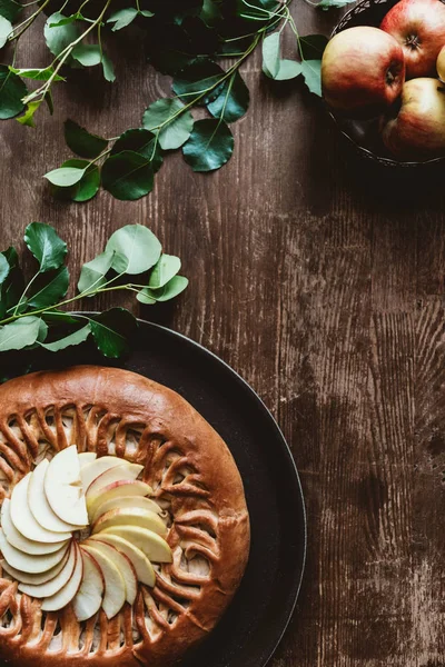 Vista superior de torta de maçã caseira e maçãs frescas com folhas verdes na mesa de madeira — Fotografia de Stock