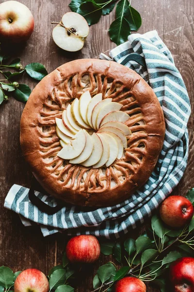 Top view of arranged apple pie and fresh apples with green leaves on wooden surface — Stock Photo