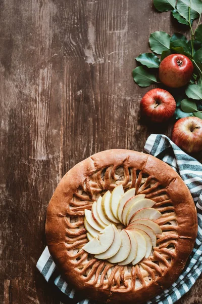 Top view of arranged apple pie and fresh apples with green leaves on wooden surface — Stock Photo