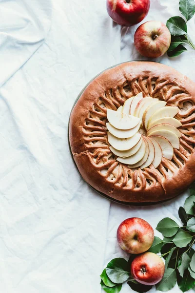 Top view of arranged apple pie, fresh apples and green leaves on white tablecloth — Stock Photo