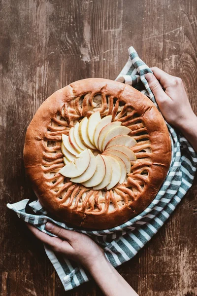 Tiro cortado de mulher com linho segurando torta de maçã caseira na placa de corte de madeira — Fotografia de Stock