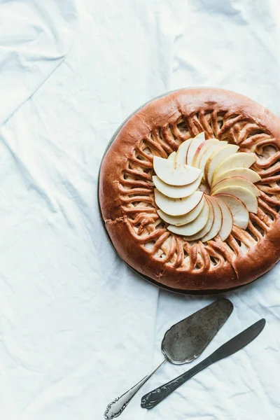 Vue du dessus de tarte aux pommes maison, serveur de gâteaux et couteau sur nappe blanche — Photo de stock