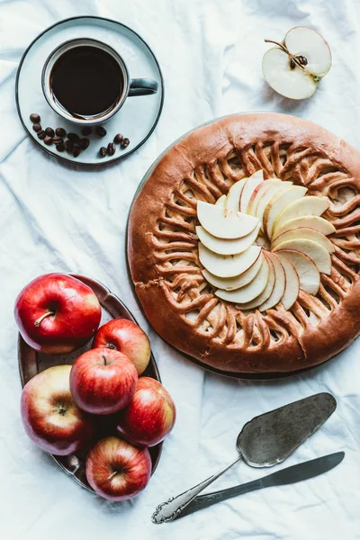 Acostado plano con taza de café, tarta de manzana y manzanas frescas en mantel blanco - foto de stock