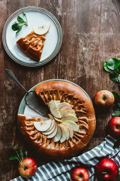 Flat lay with piece of homemade apple pie, cake server and fresh apples on wooden surface — Stock Photo