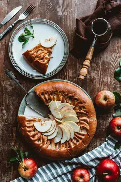 Tendido plano con pedazo de tarta de manzana casera, cubiertos y cafetera dispuestos en la superficie de madera - foto de stock