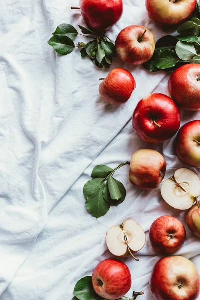 Flat lay with fresh apples and green leaves on white linen — Stock Photo