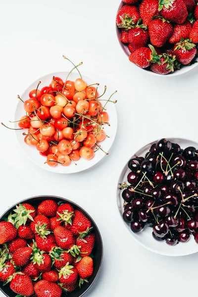 Верхний вид свежих спелых вкусных летних ягод в мисках на белом — стоковое фото