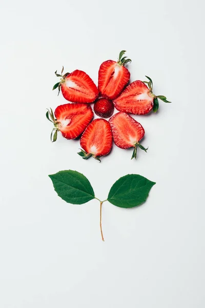 Top view of flower made of sliced strawberries and green leaves on white — Stock Photo