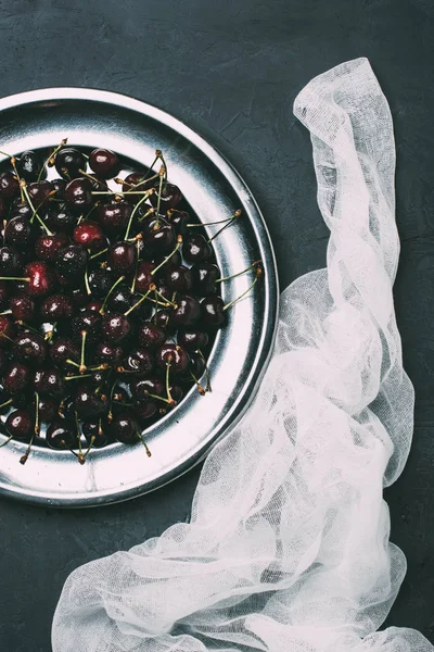 Vista dall'alto di ciliegie dolci fresche su piastra in metallo lucido e tessuto su nero — Foto stock