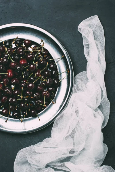 Vue de dessus des cerises douces fraîches sur plaque métallique brillante et tissu sur noir — Photo de stock