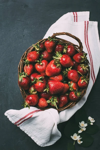 Top view of fresh ripe sweet strawberries in wicker basket and towel on black — Stock Photo