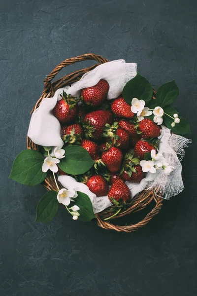 Vista superior de fresas frescas maduras y hermosas flores de jazmín en cesta en negro - foto de stock