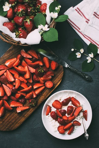 Top view of sliced strawberries on wooden cutting board, cottage cheese and jasmine flowers on black — Stock Photo
