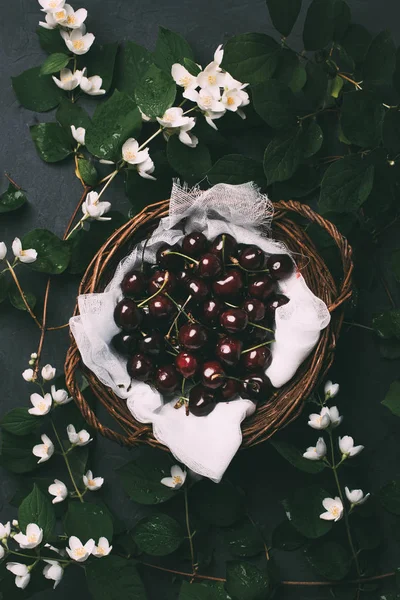 Vista superior de cerejas doces maduras em cesta e belas flores de jasmim em preto — Fotografia de Stock