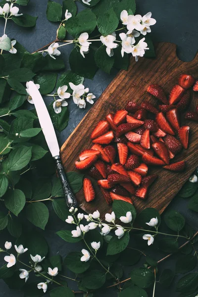 Top view of beautiful jasmine flowers, sliced strawberries on wooden cutting board and knife — Stock Photo