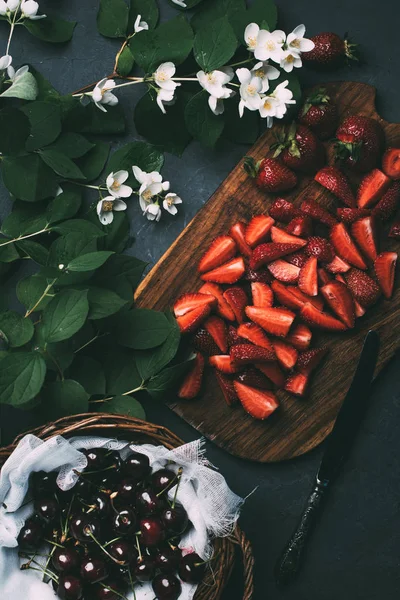 Вид зверху на красиві квіти жасмину, нарізані полуниці і стиглі солодкі вишні на чорному — стокове фото