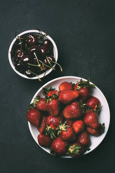 Top view of delicious strawberries and ripe sweet cherries in bowls on black — Stock Photo