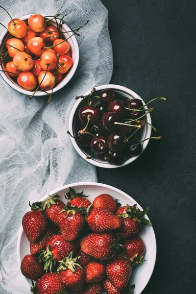 Vue de dessus des cerises douces et des fraises dans des bols sur noir — Photo de stock