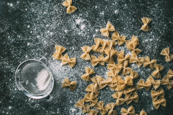 Vista elevada de macarrão farfalle e peneira na mesa coberta de farinha — Fotografia de Stock