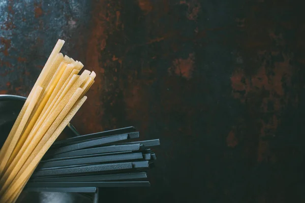 Draufsicht auf schwarze und klassische Linguine-Pasta in der Pfanne auf rustikalem Tisch — Stockfoto
