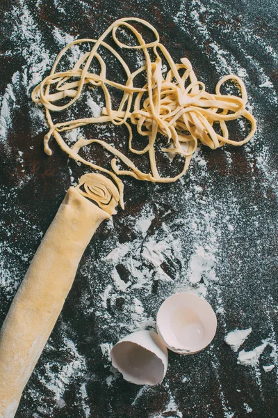 Top view of dough, egg shell and raw pasta on table covered by flour — Stock Photo