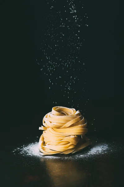 Nahaufnahme von Mehl, das auf Tagliatelle-Pasta auf schwarzem Hintergrund fällt — Stockfoto