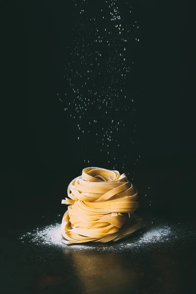 Крупный план муки падающей на пасту Tagliatelle на черном фоне — стоковое фото