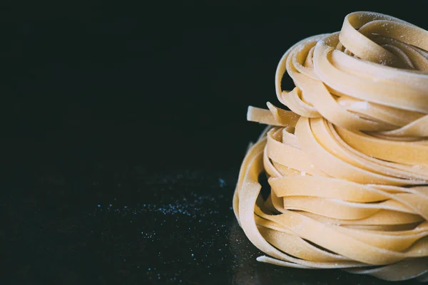 Closeup view of raw tagliatelle pasta covered by flour on black background — Stock Photo