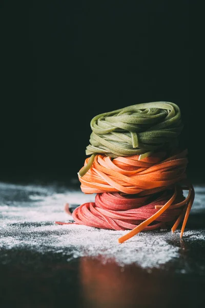 Primer plano de pila de pasta tagliatelle colorido crudo en la mesa cubierta por harina - foto de stock